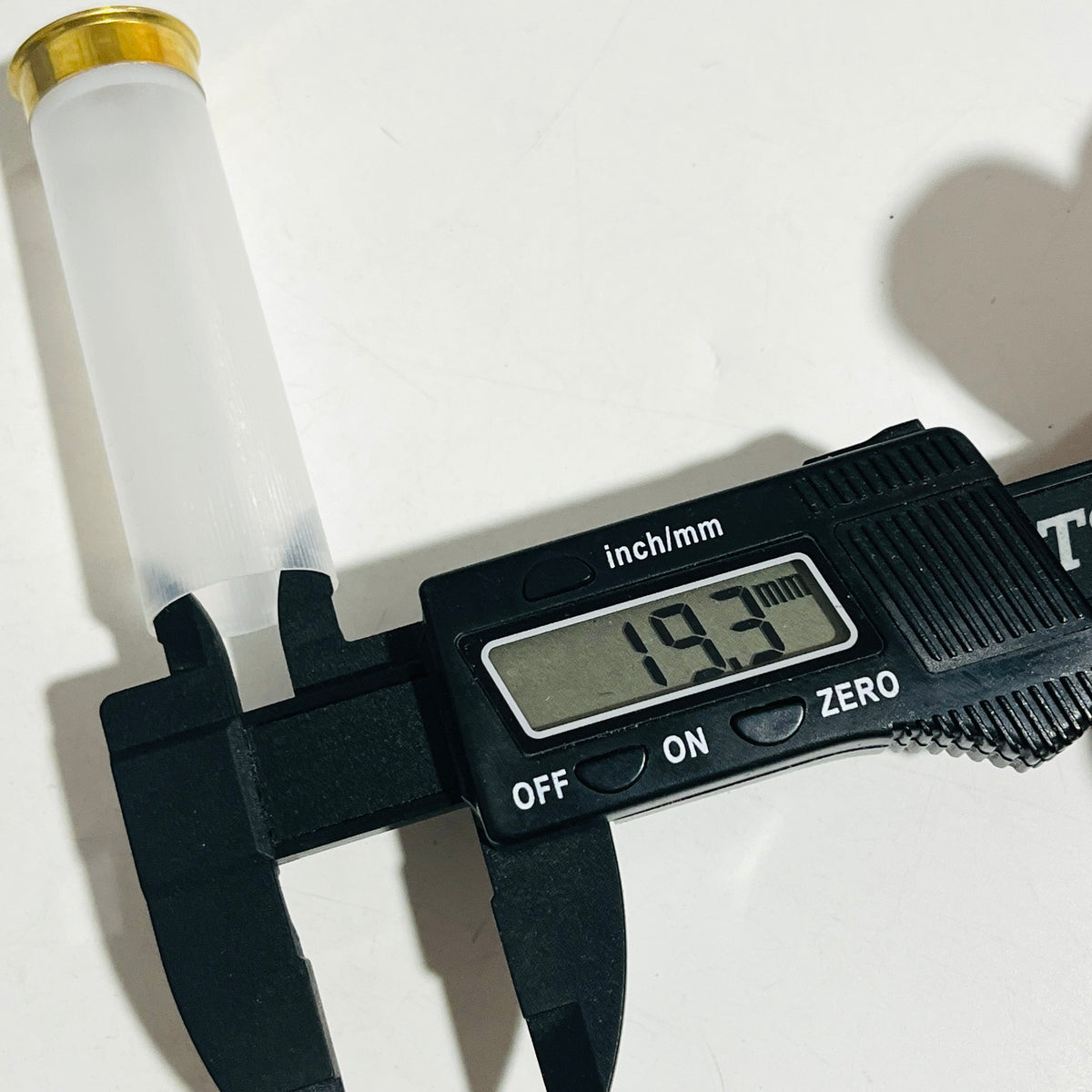 Digital caliper reading 19.3 mm across the plastic body of a clear, empty 12 gauge shotshell with a brass head