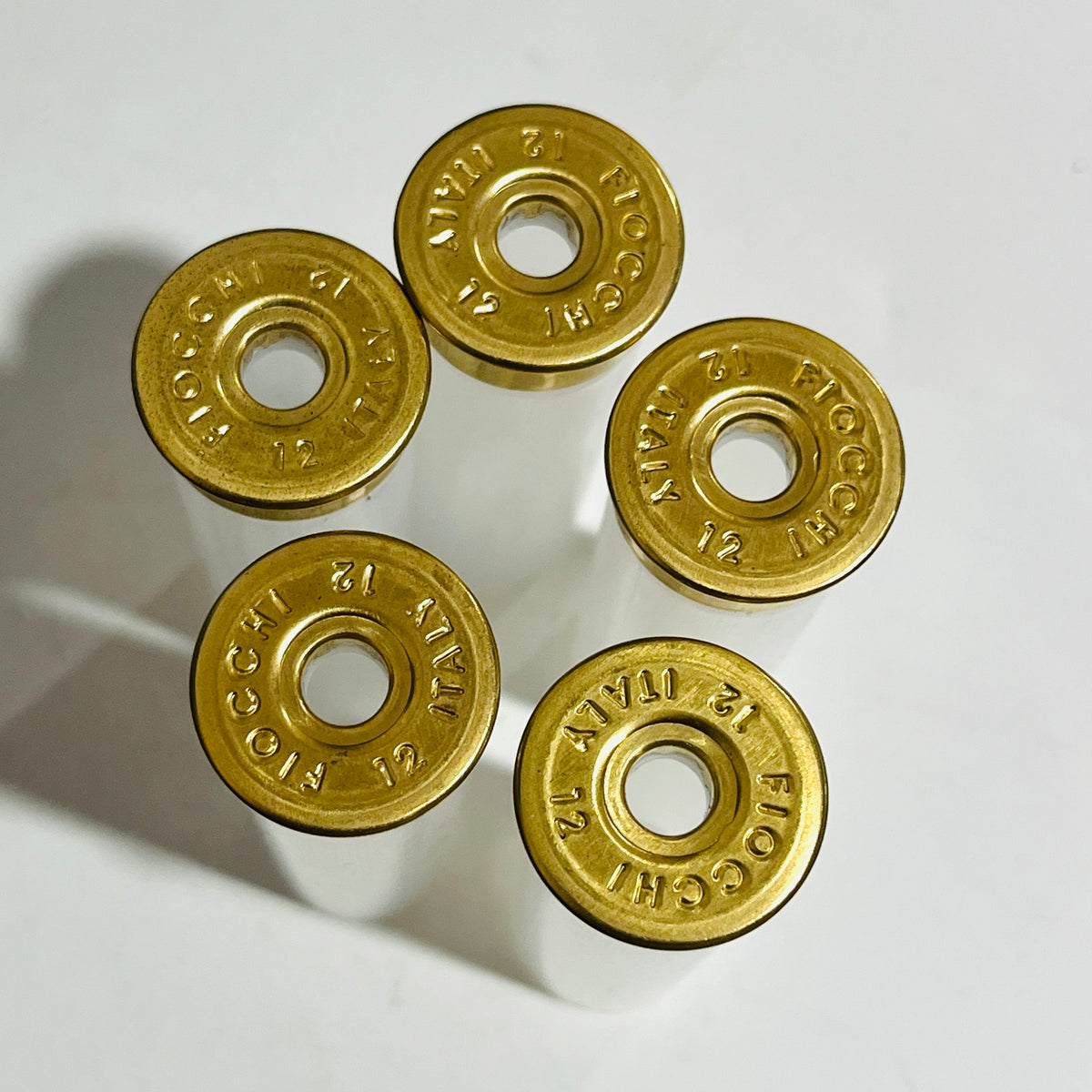 Top-down view of five empty shotshells standing upright, brass heads stamped FIOCCHI 12 ITALY around open primer pockets
