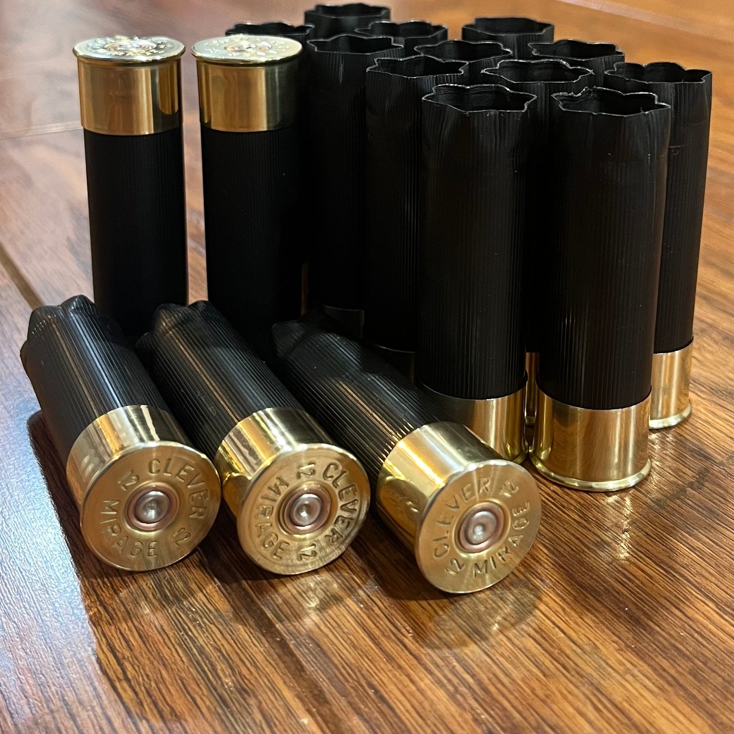 A large group of  unmarked black shotgun shells, some open-ended, three showing Clever Mirage headstamps on a wood table