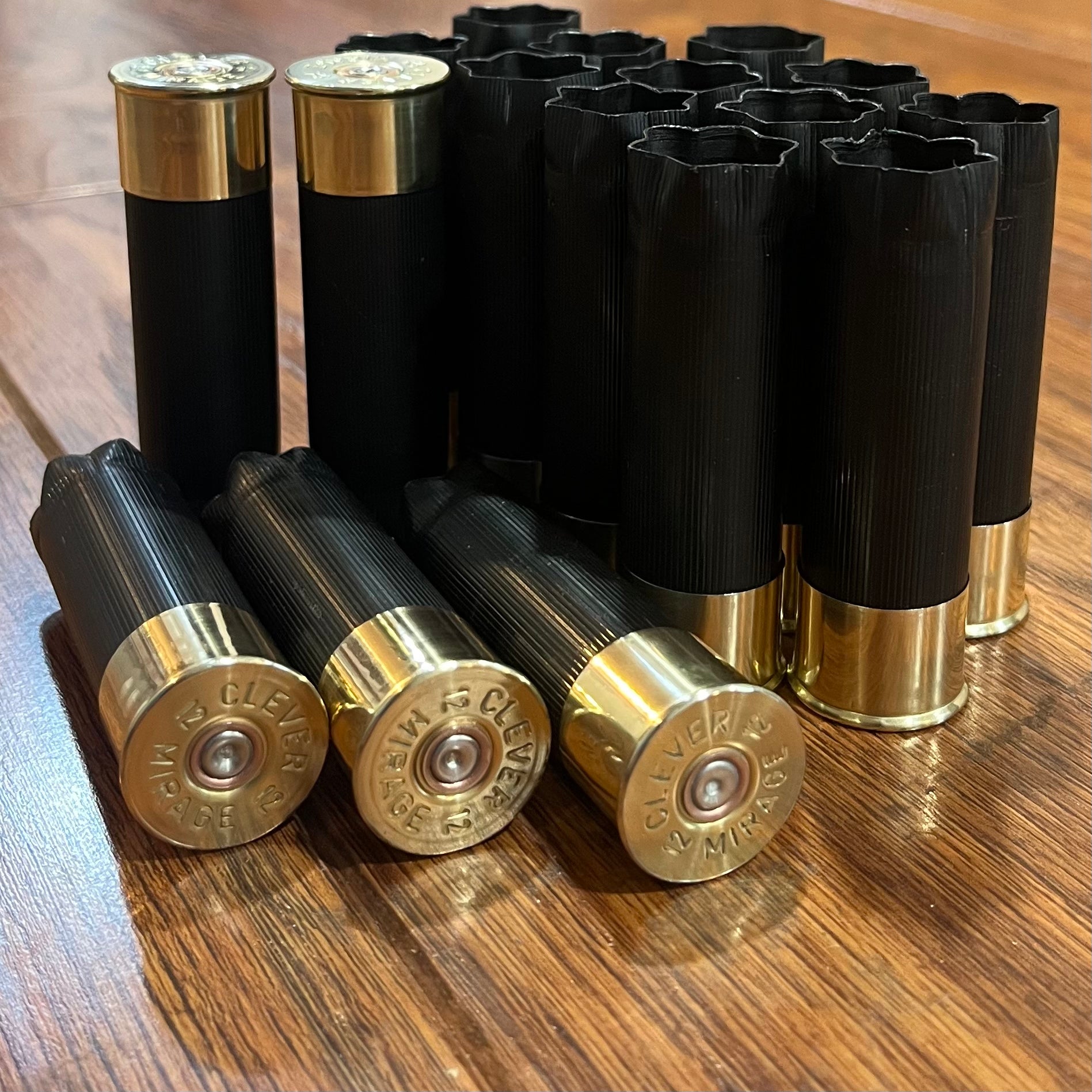 A large group of  unmarked black shotgun shells, some open-ended, three showing Clever Mirage headstamps on a wood table