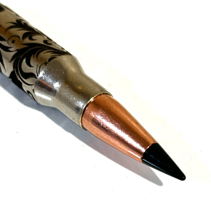 Close-up view of a single nickel bullet casing showcasing intricate Baroque scroll engraving and a prominent black projectile tip