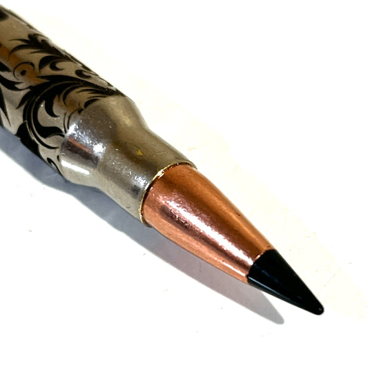 Close-up view of a single nickel bullet casing showcasing intricate Baroque scroll engraving and a prominent black projectile tip