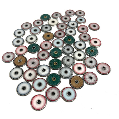 A pile of silver-rimmed shotgun shell slices showing colorful plastic wad centers in white, blue, green, and tan