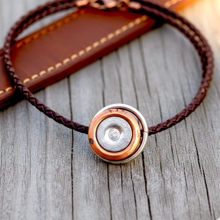 A braided brown leather bracelet featuring a central round silver and copper craft primers component.