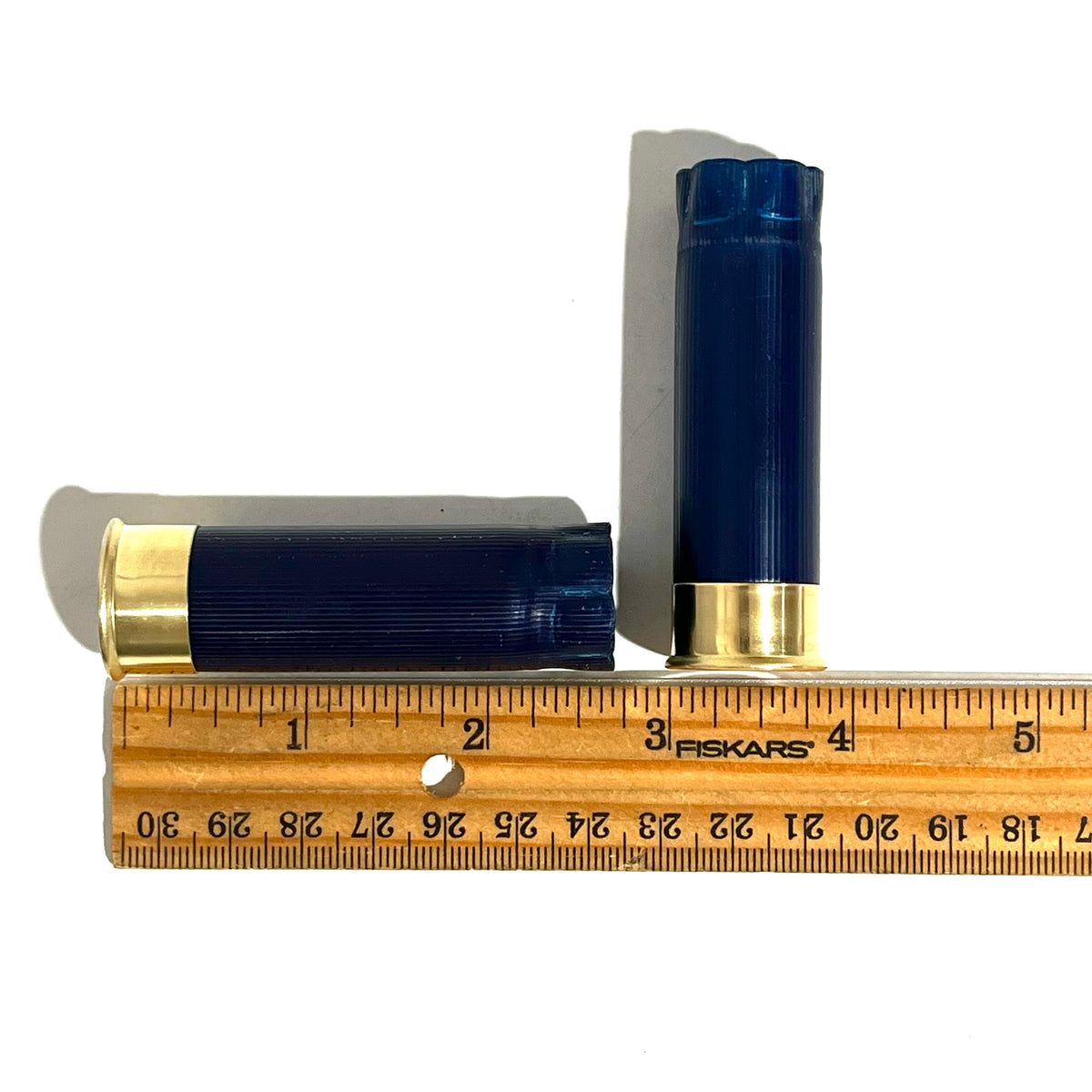 Two dark blue 12 gauge shotgun shells with gold bases measured against a ruler showing approximately 2.75 inches