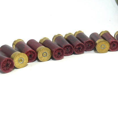 Row of dark red 12 gauge dummy shotgun shells with gold bases lying on white background