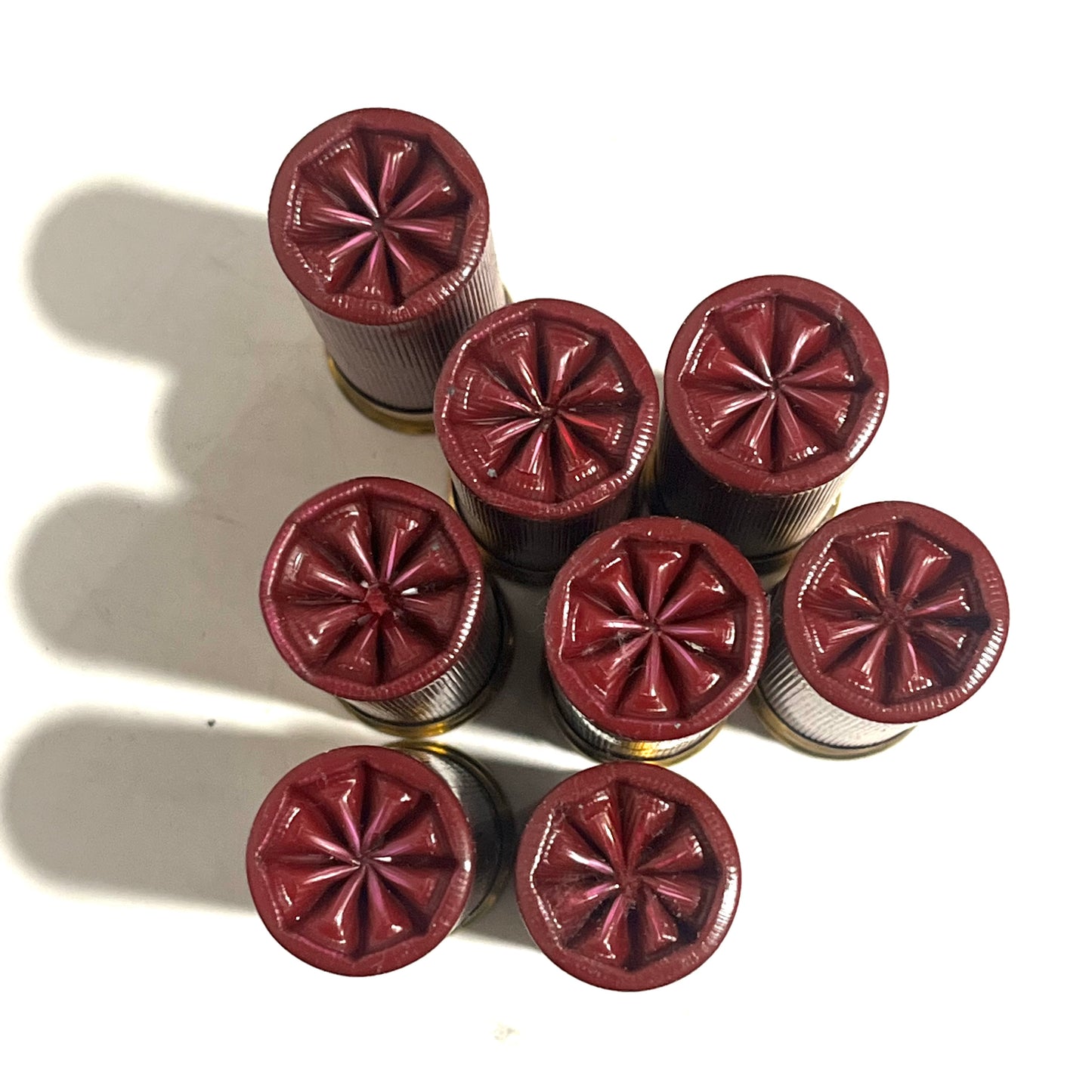 Overhead view of 8 dark red 12 gauge dummy shotgun shells with star crimped tops arranged in a cluster