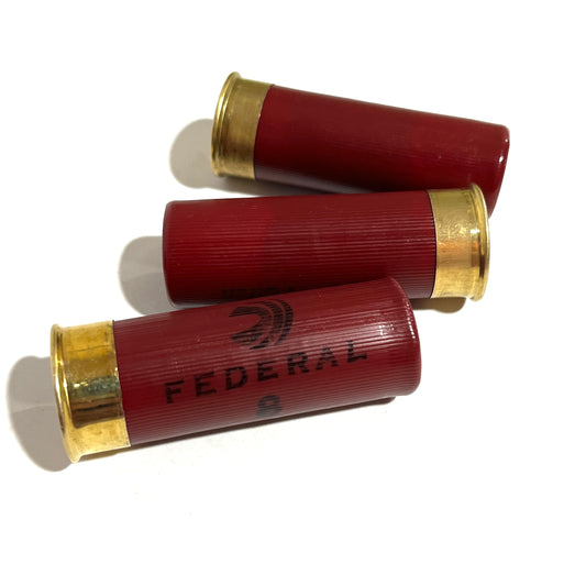 Three dark red Federal 12 gauge dummy shotgun shells with gold brass bases fanned out on white background
