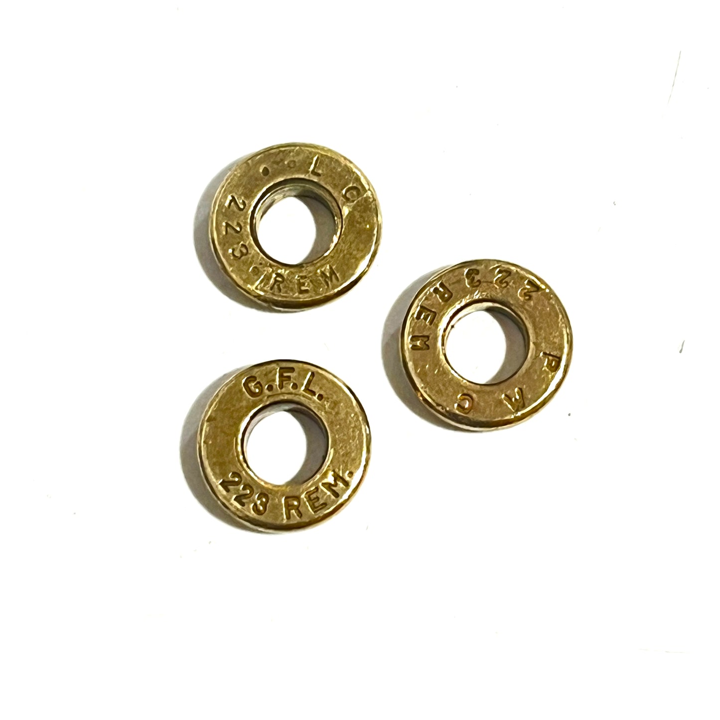 3 brass deprimed bullet slices with donut shape showing headstamps reading 223 REM and G.F.L. 223 REM on a white background