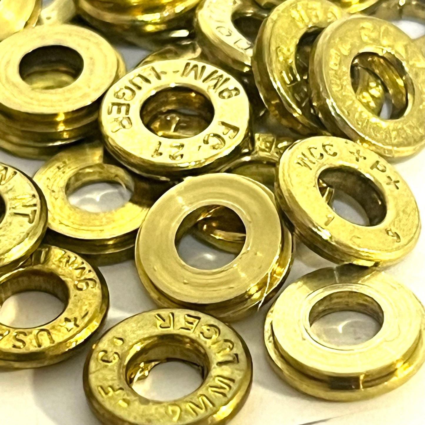 A tightly packed pile of deprimed 9mm brass slices with hollow centers, showing multiple legible manufacturer headstamps.