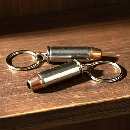 Two handmade bullet keychains made from nickel 38 Special casings with copper round nose bullets on a wooden surface.