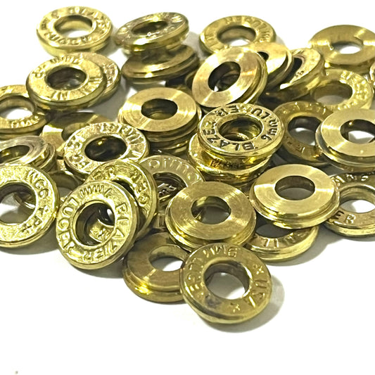 Large pile of gold brass deprimed bullet slices with visible caliber headstamps including Luger and Blazer on a white background