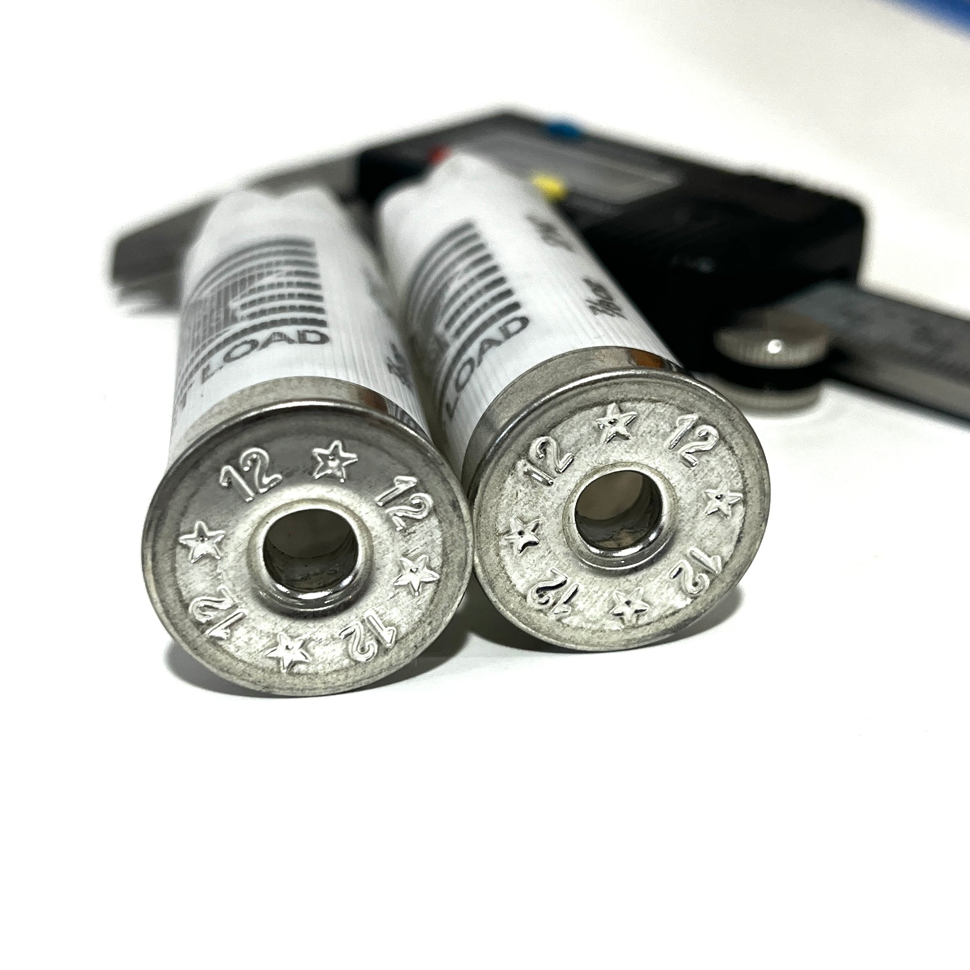 Close-up of two deprimed white Stars and Stripes 12 gauge shotgun shell bases showing empty primer holes next to a caliper
