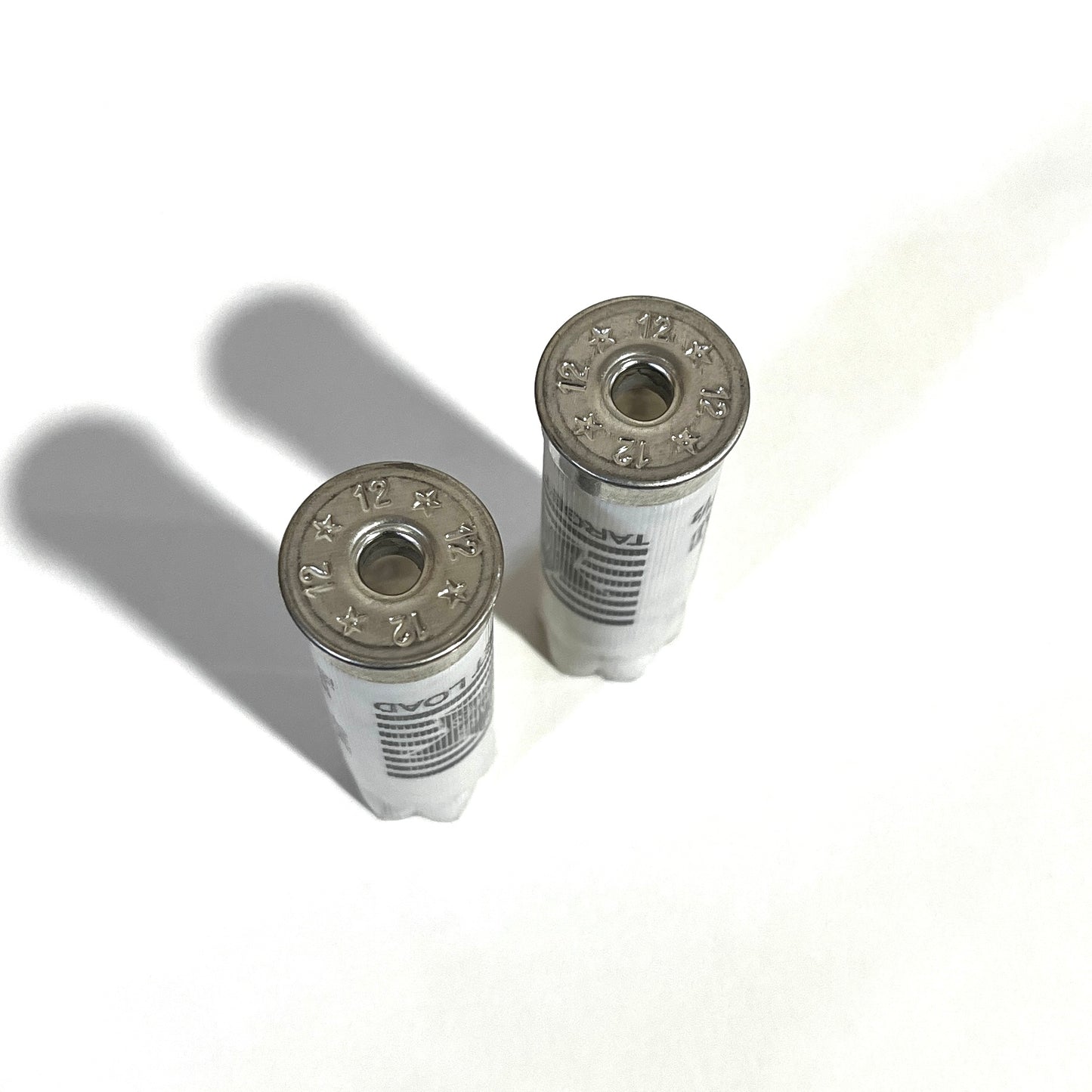 Two deprimed white Stars and Stripes 12 gauge shotgun shells viewed from above showing empty primer holes