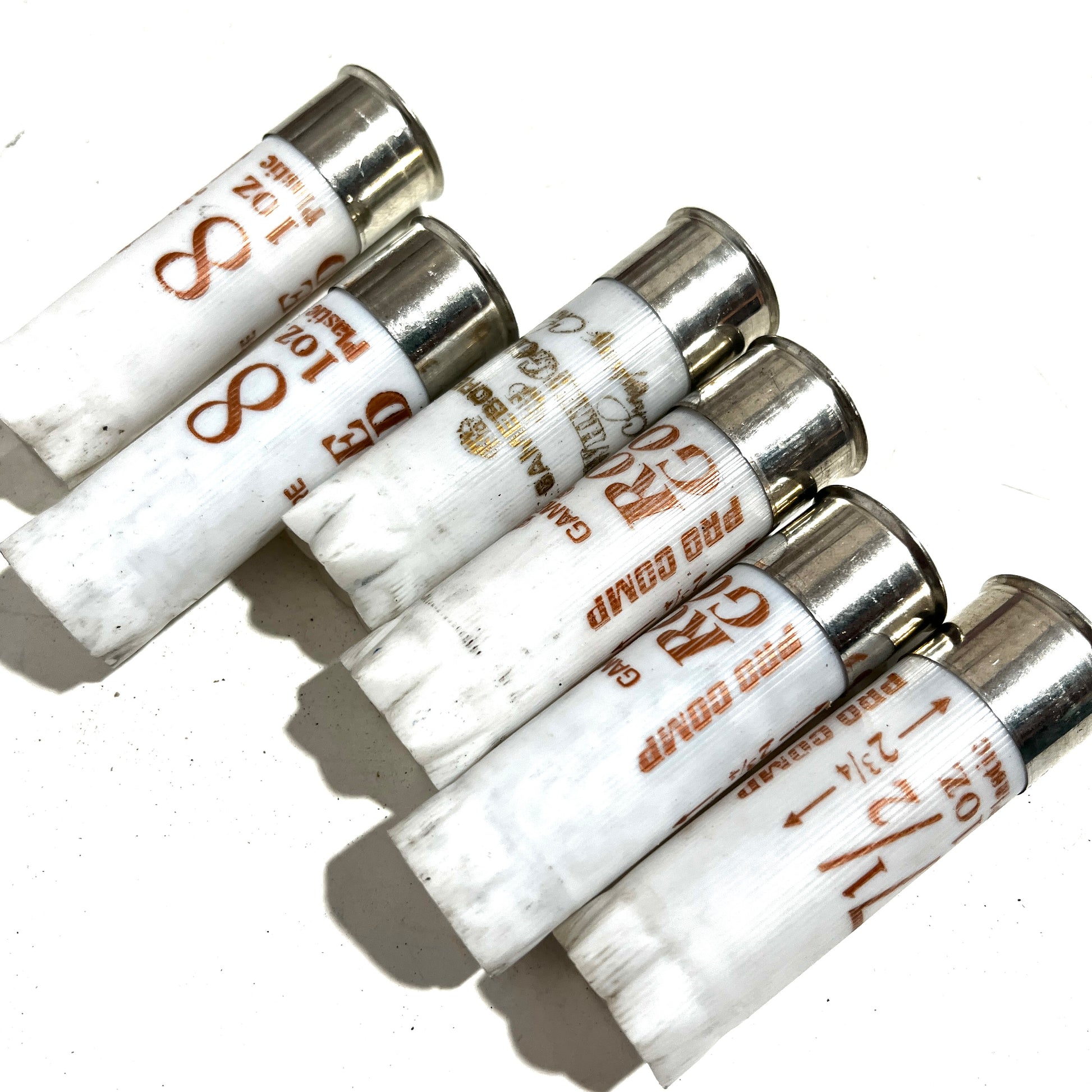 A row of six white Gamebore 12 gauge empty shotgun shells lined up diagonally on a white background, highlighting the silver bases and printed load details.

