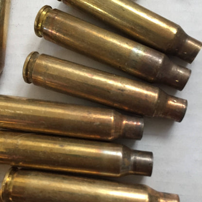 Six uncleaned 223 spent brass cases stacked horizontally in parallel showing shoulder tarnish and neck discoloration.