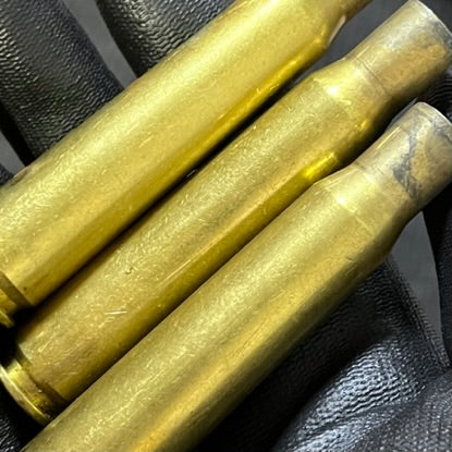 Three dirty 50 BMG rifle cases lying across a black gloved hand, showing natural carbon tarnish on the shoulder.