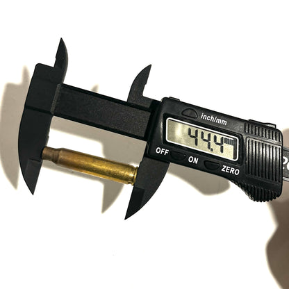 Black digital caliper measuring overall length of an uncleaned 223 brass casing, displaying 44.47 mm.