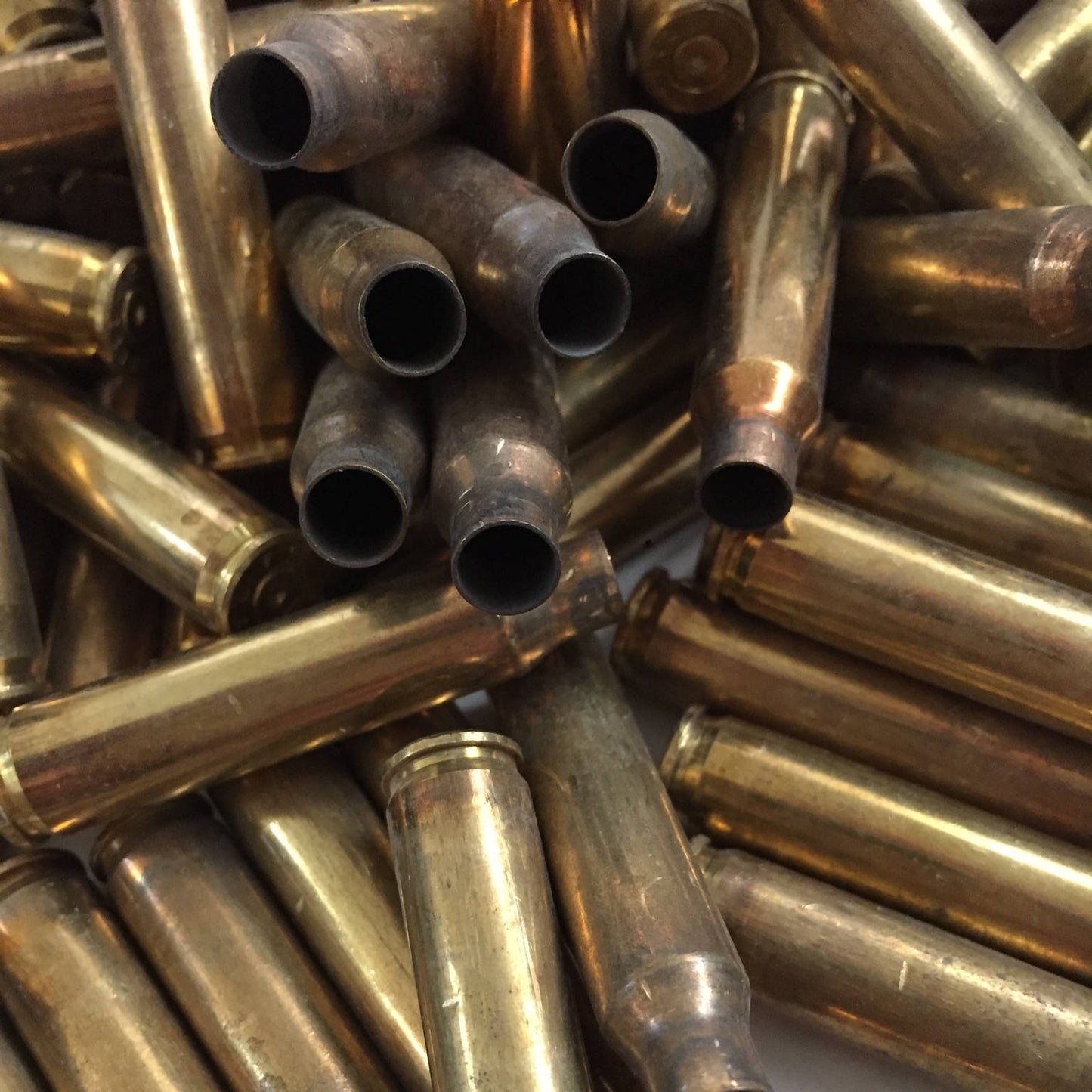 Close-up view of dark open mouths on a cluster of uncleaned 5.56 brass cartridge cases in a layered pile.