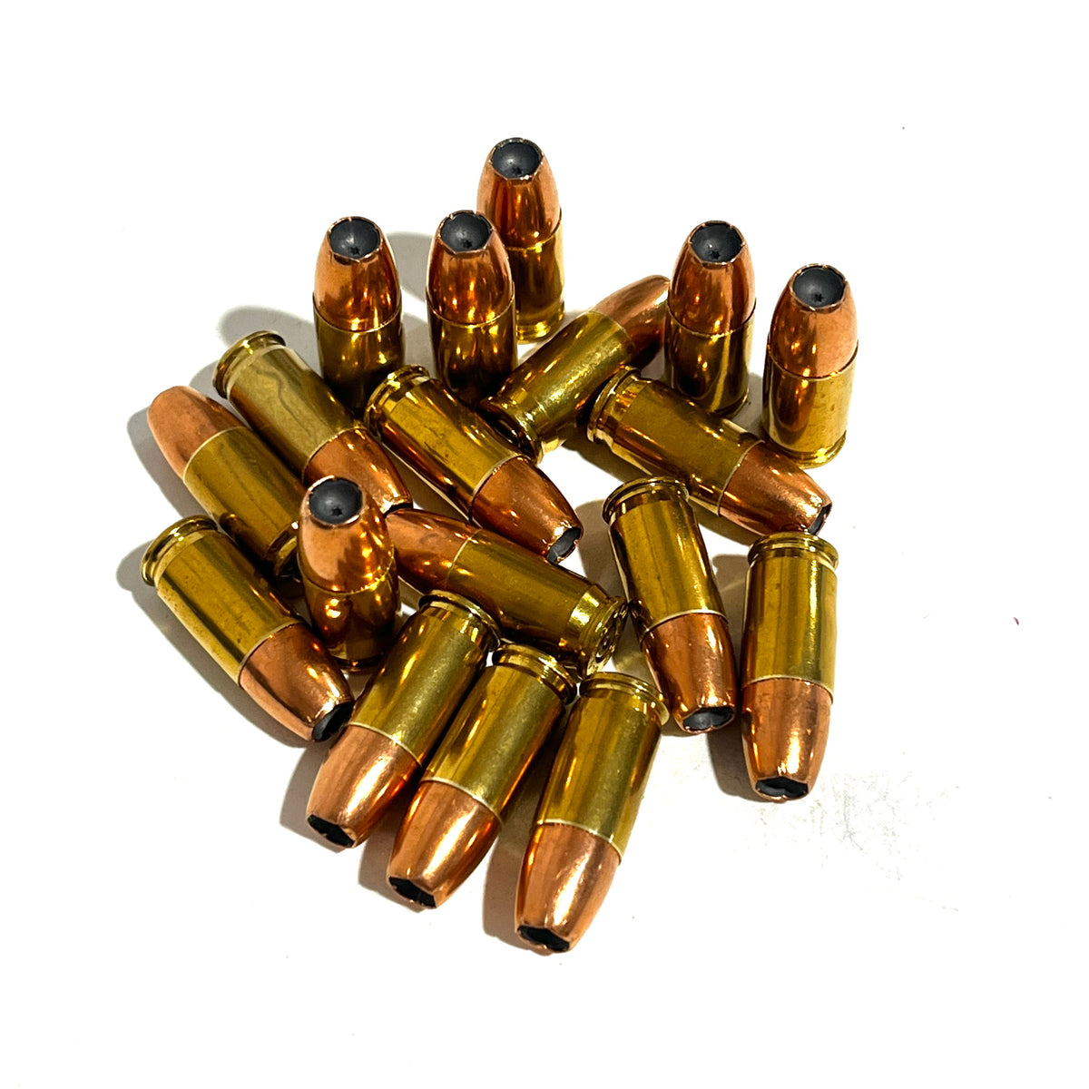 Pile of dummy .380 Auto rounds with copper jacketed hollow point bullets and brass casings on white background