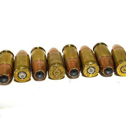 8 dummy .380 Auto rounds laid in a row showing brass headstamps and hollow point bullet tips