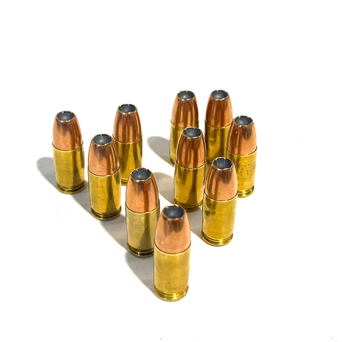 9 dummy .380 Auto rounds standing upright in cluster on white background, hollow point bullets facing up