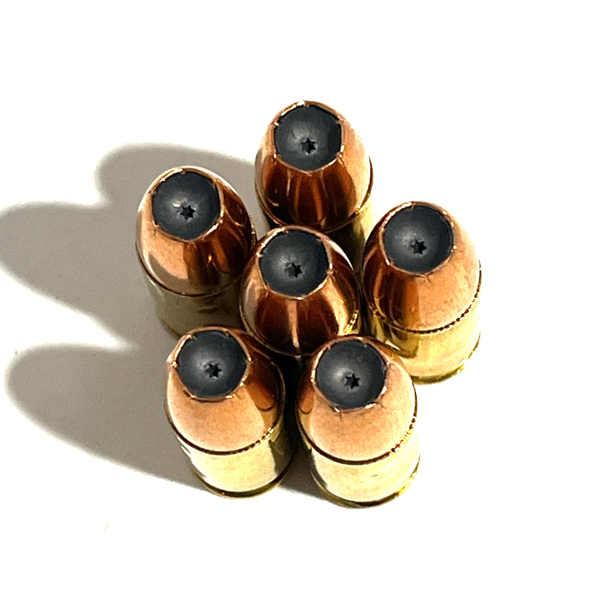 6 dummy .380 Auto rounds viewed from bullet tip, hollow point cavities visible, brass casings behind