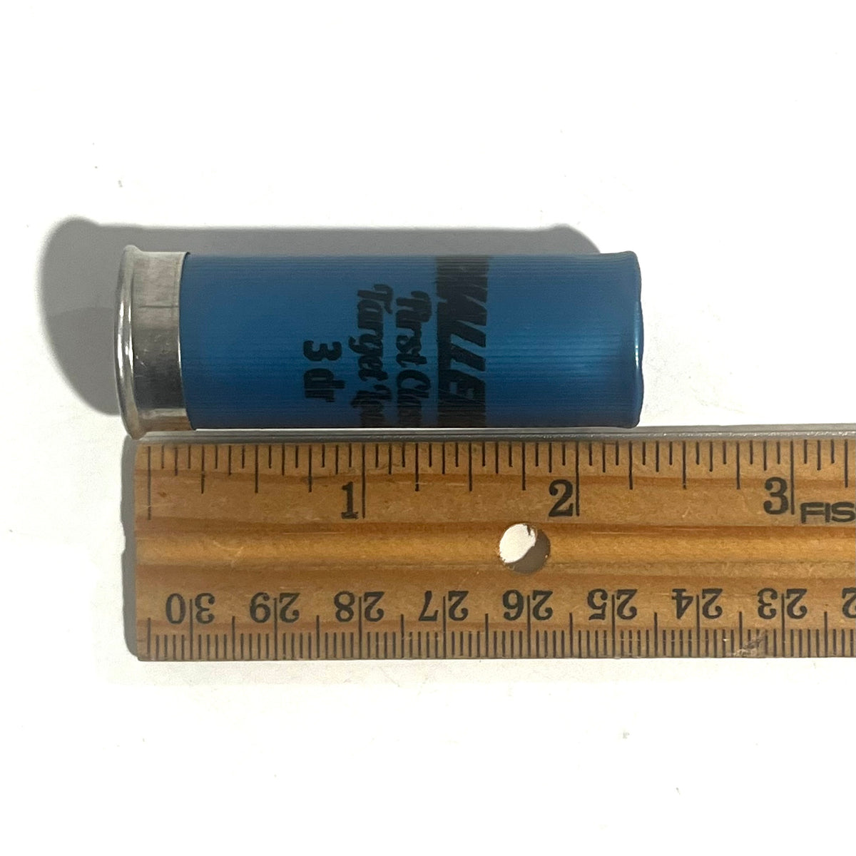A blue Challenger First Class Target Load shotgun shell beside a ruler showing a length of about 2.75 inches