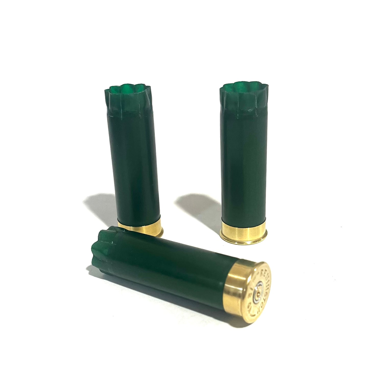 Three emerald green shotgun shells with gold bottoms with one lying on its side showing the primer