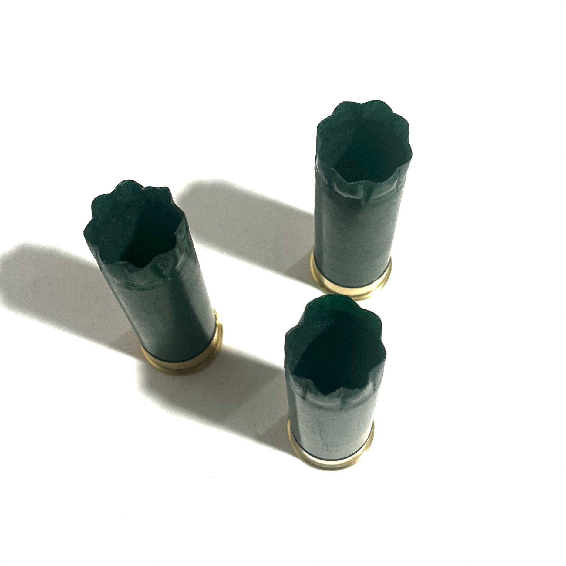 Three emerald green shotgun shells with gold bottoms viewed from above showing crimped star tops