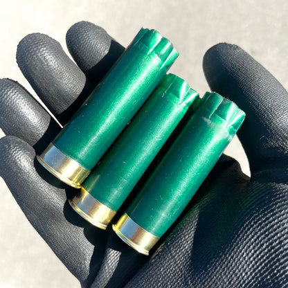 Three emerald green shotgun shells with gold bottoms held in a black gloved hand