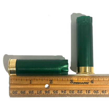 Two emerald green shotgun shells with gold bottoms beside a ruler showing a length of about 2.75 inches