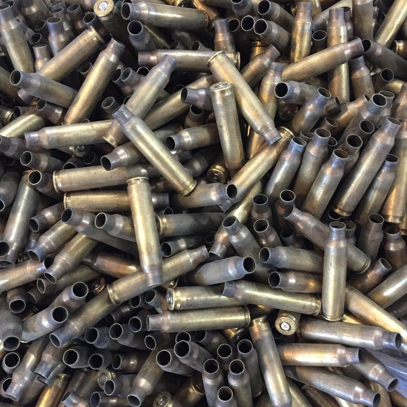 Direct overhead view of a large, dense pile of uncleaned 223 spent brass casings showing open mouths and base rims.
