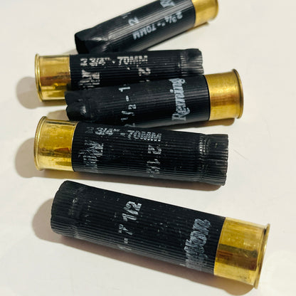 Five empty black shotgun hulls with brass bases scattered on a white surface, printed 2 3/4" - 70MM