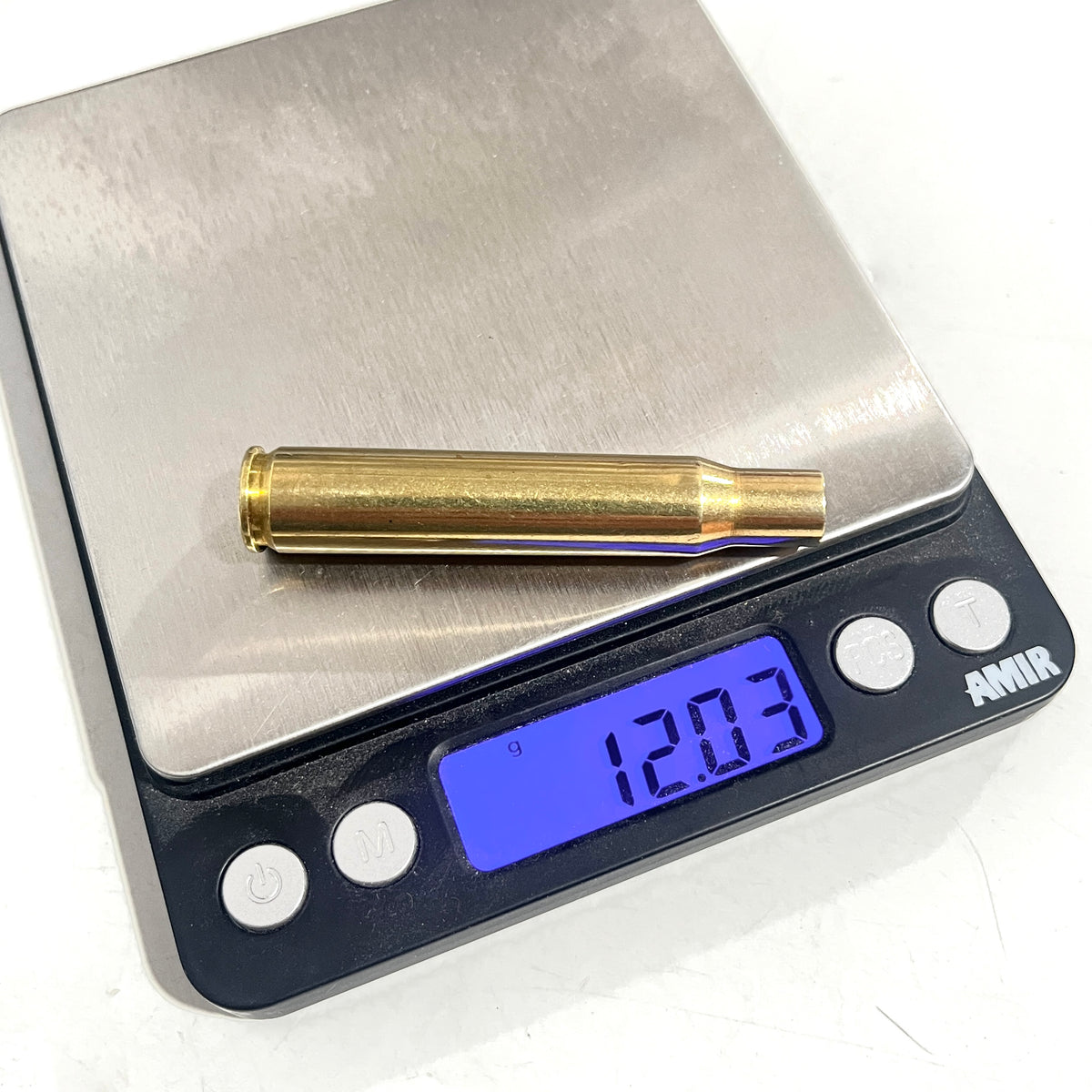 A single empty brass rifle casing lying on a digital scale that displays a weight of 12.03 grams.
