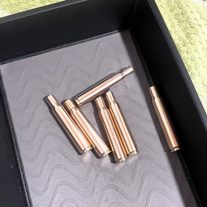 Several brass empty rifle casings lying inside a textured grey tray with a thick black rim.
