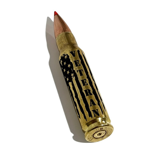 Engraved brass .308 WIN cartridge lying diagonally, showing red tip and headstamp markings