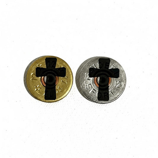 Two thin-cut, once-fired 12-gauge shotgun shell slices (one gold, one silver) featuring an engraved black cross silhouette in the center against a white background.

