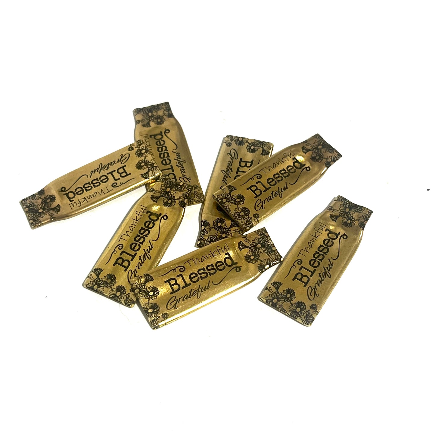 Group of flattened gold-brass .308 casings showing variations in shape and floral engraving placement
