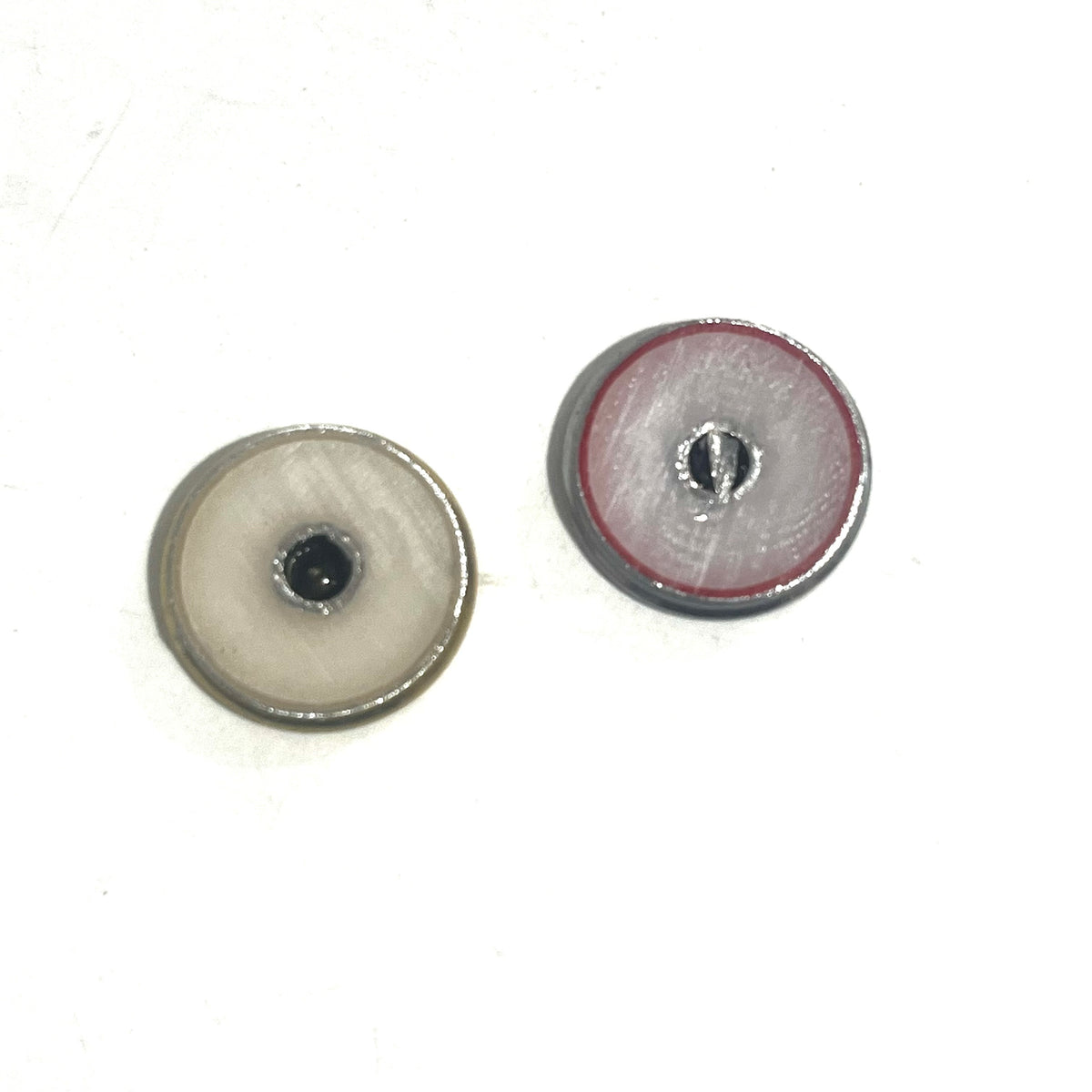 2 round shotgun shell slices viewed from the underside showing white enamel-lined centers, one with gray edging and one with red edging