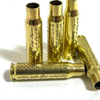 Five engraved brass 308 WIN once-fired cartridges, three standing and two lying on a white background