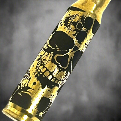 Close-up diagonal view of laser-etched skull artwork on a 308 WIN brass case against a grey background.