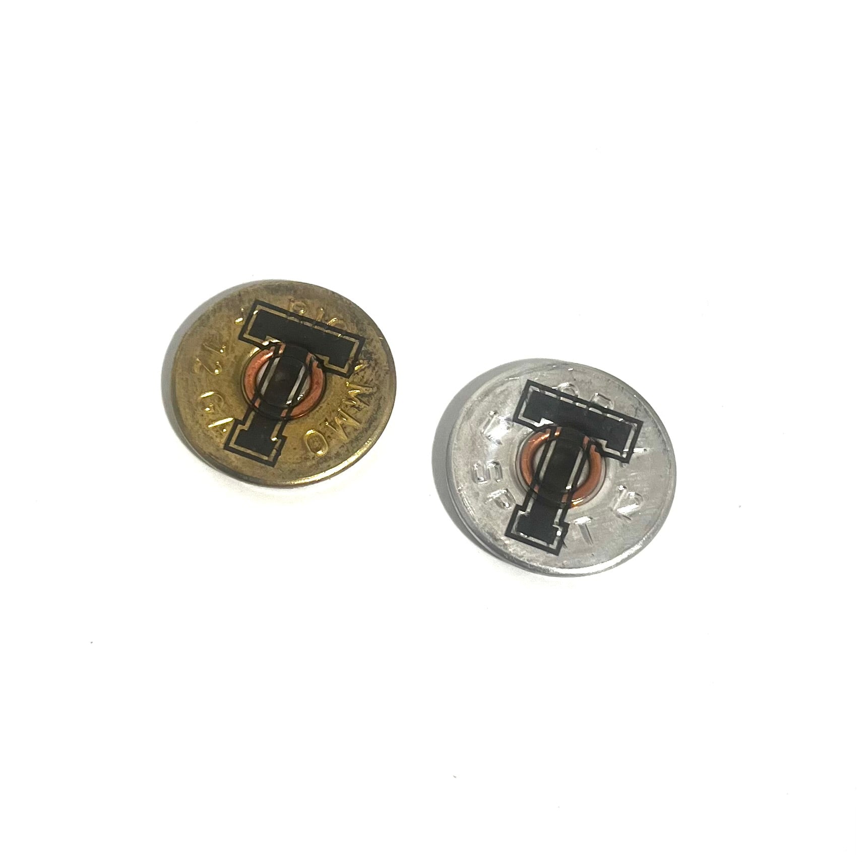 2 round 12 gauge shotgun shell slices engraved with a large letter T, one gold brass and one silver, angled view on white background