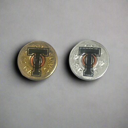 2 round 12 gauge shotgun shell slices engraved with a large letter T, one gold brass and one silver, on a gray background