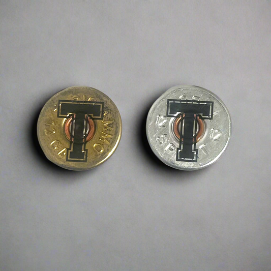 2 round 12 gauge shotgun shell slices engraved with a large letter T, one gold brass and one silver, on a gray background