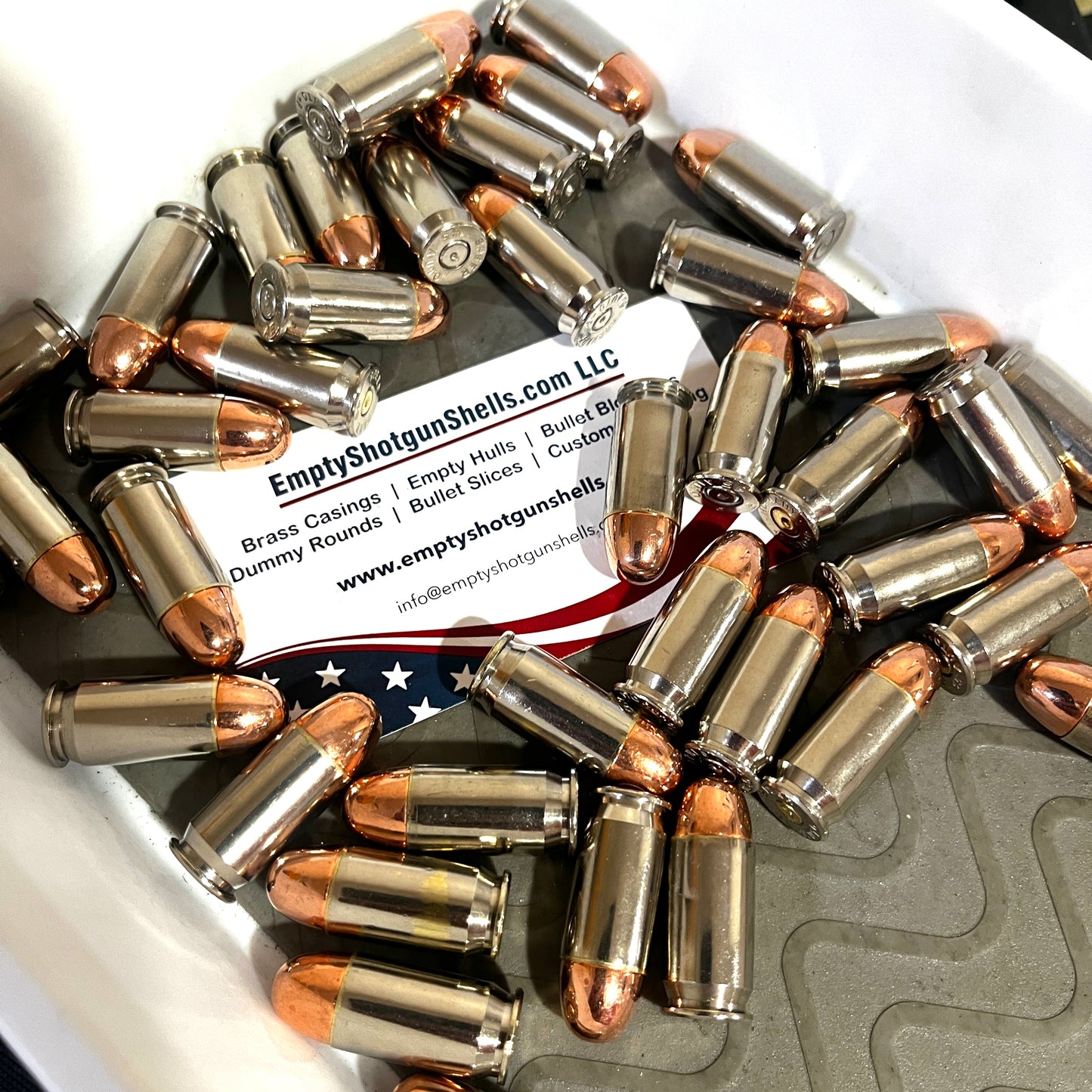 Scattered pile of fake 45 caliber bullets on a business card with a blurred American flag background.