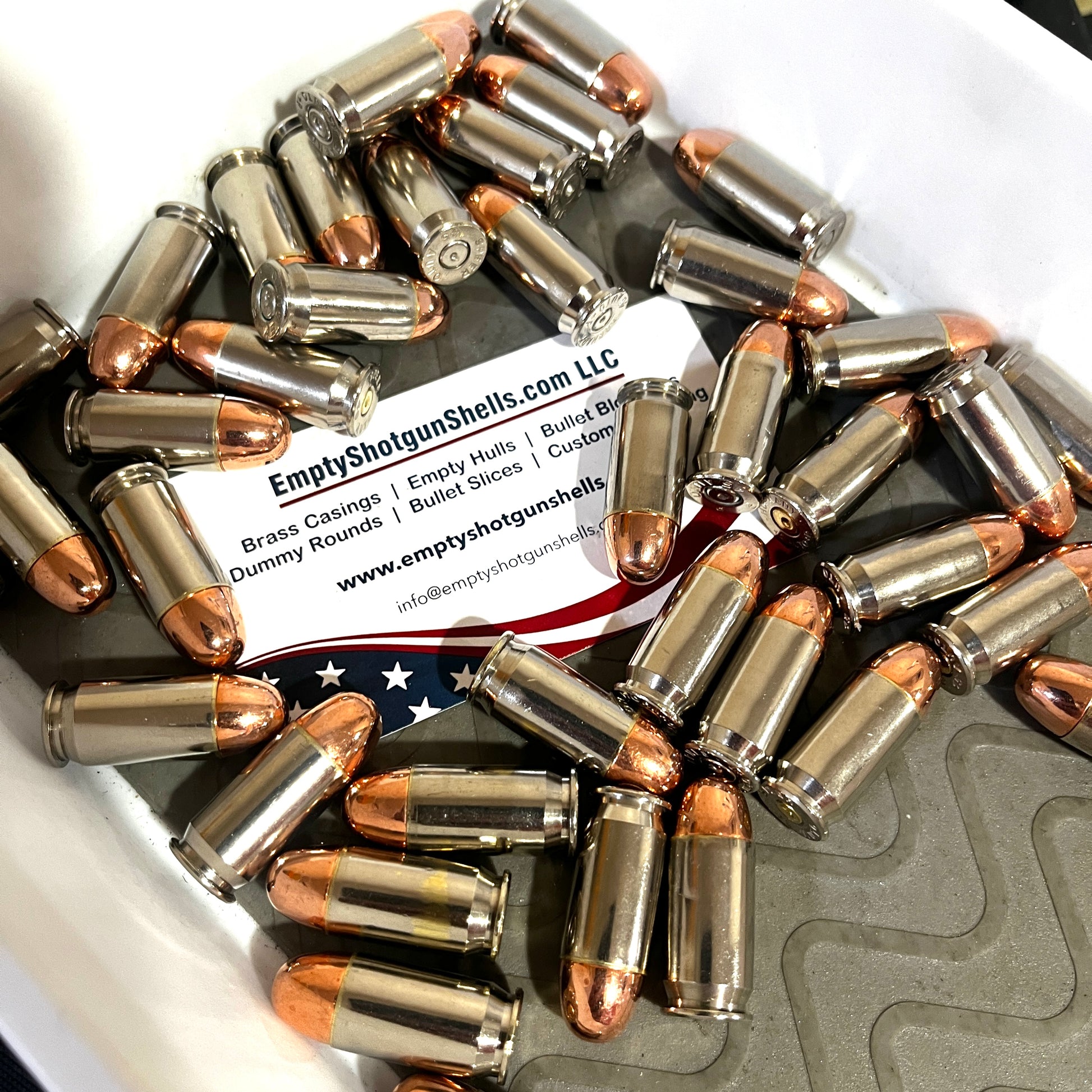 Scattered pile of fake 45 caliber bullets on a business card with a blurred American flag background.