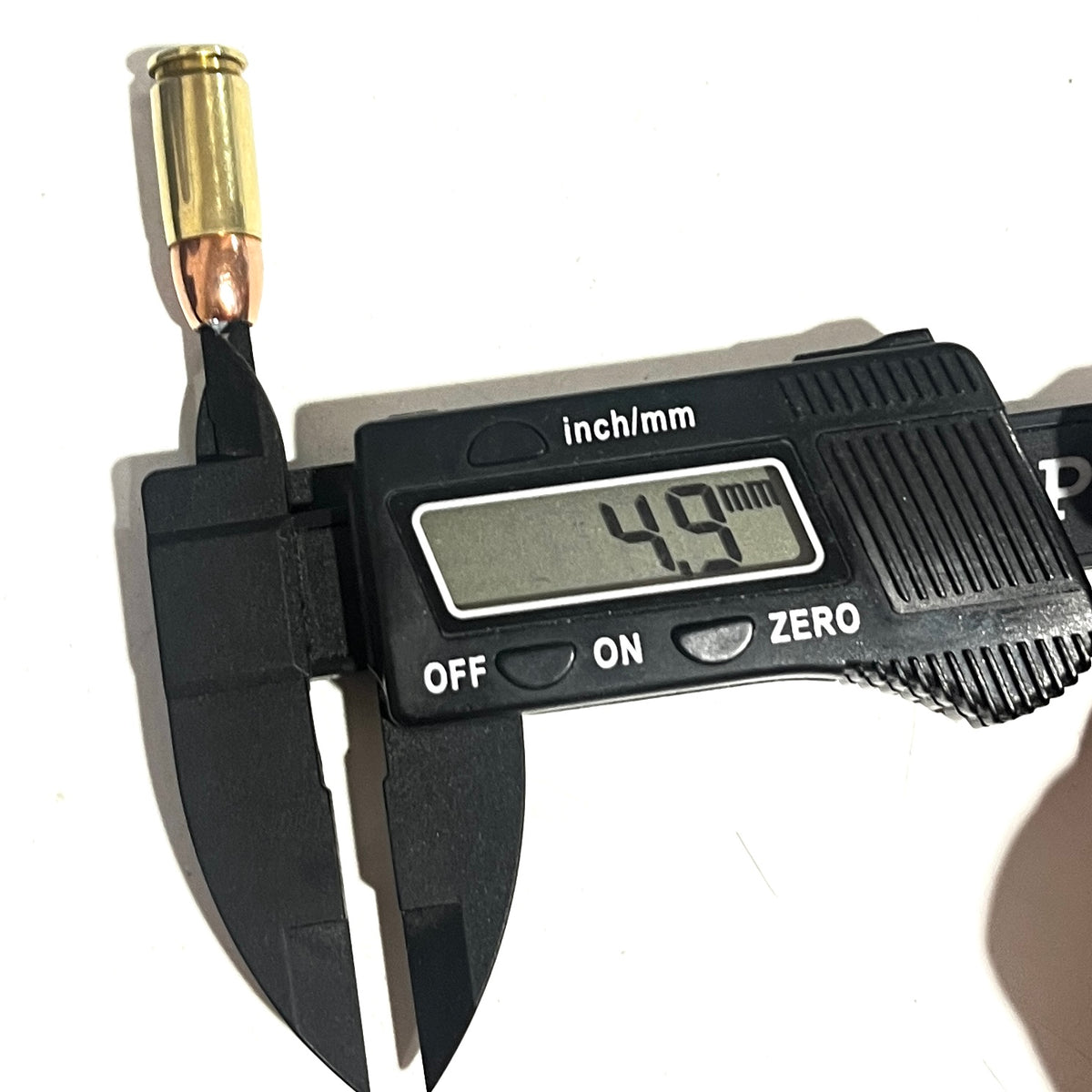A black digital caliper measuring a fake dummy round bullet opening, with the display reading 4.9 mm.