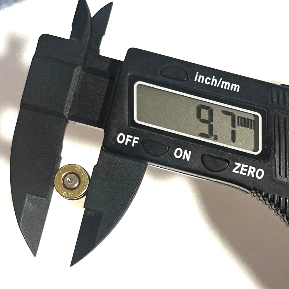 A black digital caliper measuring the fake dummy round diameter  against a plain white background, with the display reading 9.7 mm.