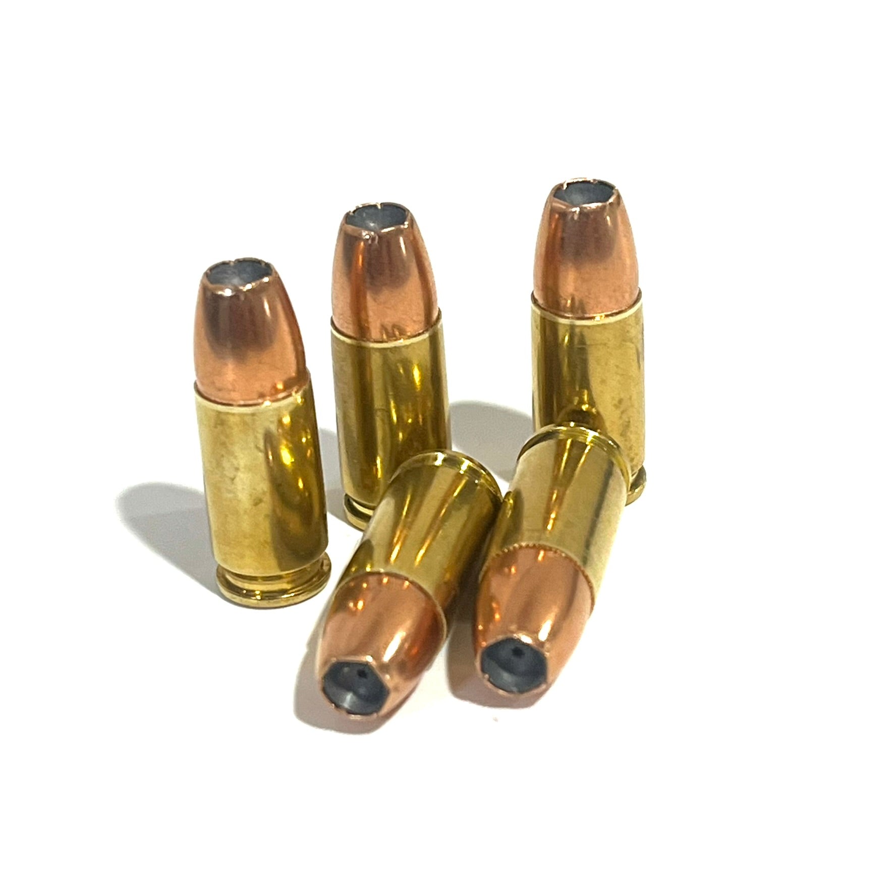 Five fake 9mm pistol rounds with jacketed hollow point bullets arranged on white with three standing and two lying down.